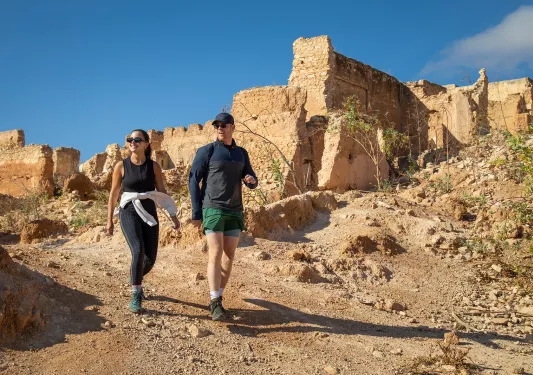 Man and woman walking on a dirt trail with ruins in the background