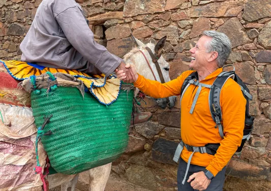 Man smiling while giving a handshake to a man riding a horse