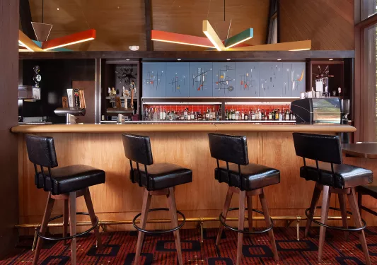 Bar and lounge with black, leather stools in front of a counter