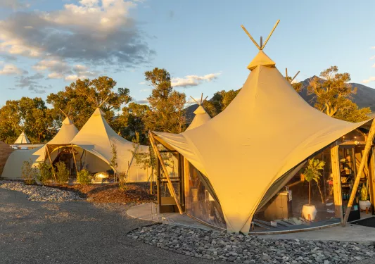 Two large, luxury tents with taller trees in the background