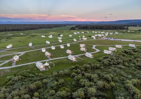 Multiple luxury tents spread across a large valley, with the sunset in the distance