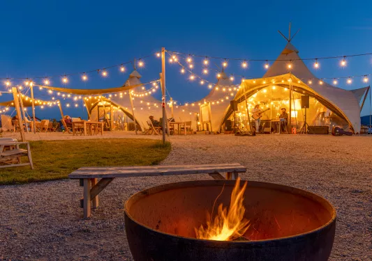 Two large luxury tents with string lights, and a fire pit in front