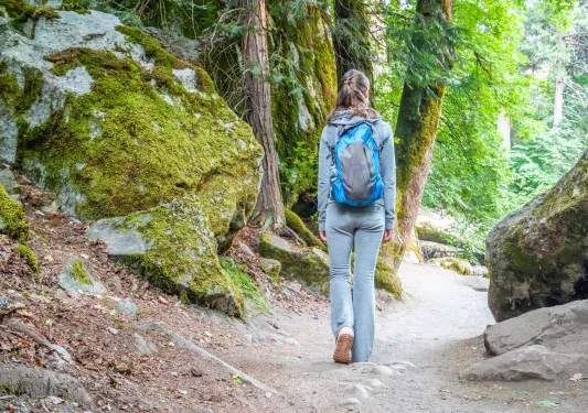 Woman wearing a backpack, walking through a dirt trail in a forest