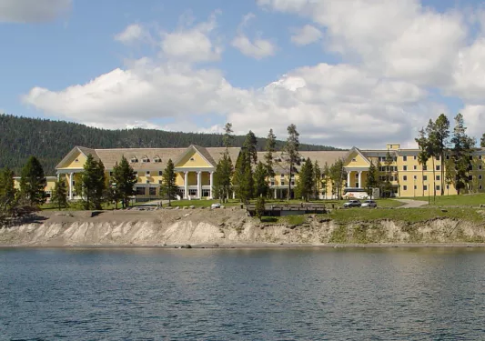 Exterior view of large, yellow building with trees and a lake in front