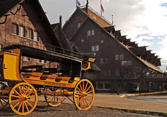 Old-style black and yellow wagon in front of a large, wooden cabin building