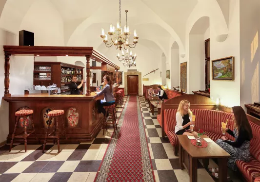 Bar and lounge with people sitting in cushioned booths, raises glasses of alcoholic beverages
