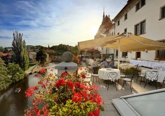 Outdoor patio and dining area in front of a white building, with a river in the distance
