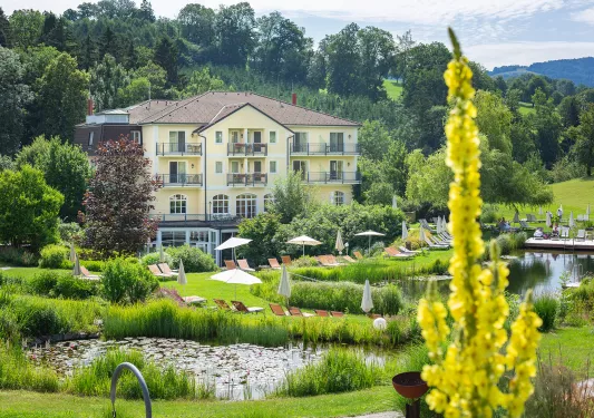 Exterior view of large, yellow hotel building with a large garden and fountain in front