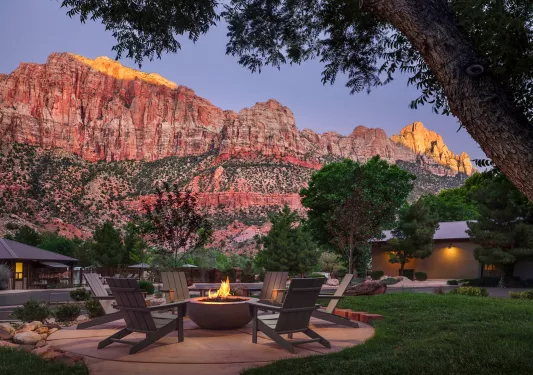 Outdoor patio with chairs surrounding a firepit with large mountains in the background