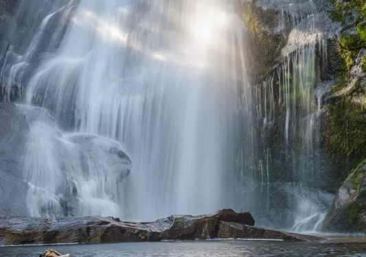 Large waterfall with a lake on the ground level, being hit by the sunlight
