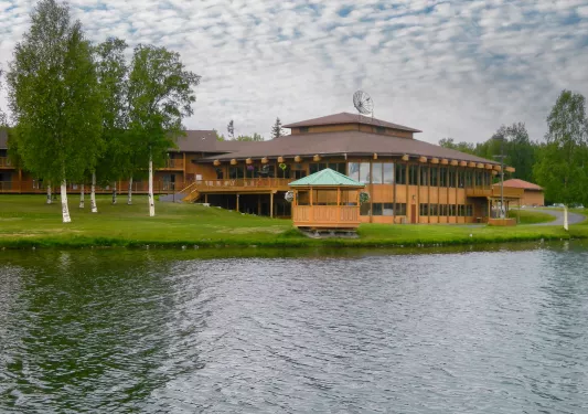 Large cabin-styled building in front of a lake with a grass field
