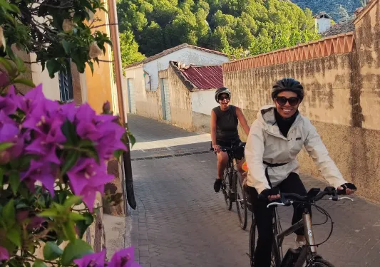 Two people biking in an alley with orange buildings behind them