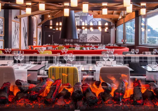 Restaurant dining hall with long tables and cushioned chairs, with light fixtures from the ceilings