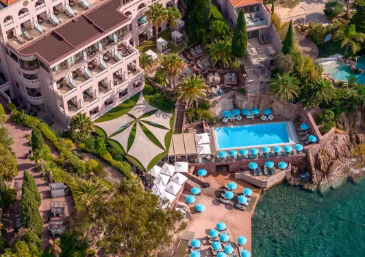 Sky view of a hotel building with an outdoor pool and blue umbrellas