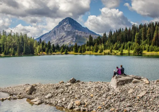 Man and woman sitting on a large boulder in front of a lake