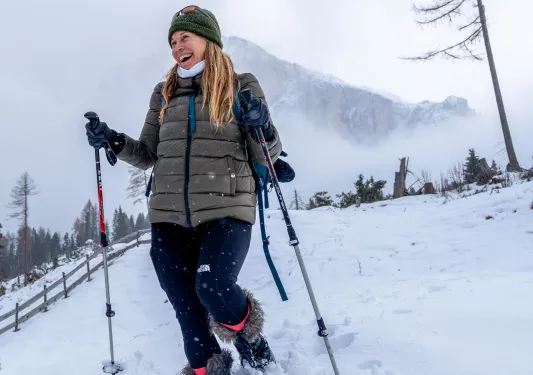 Woman smiling while walking through a snowy valley with hiking poles