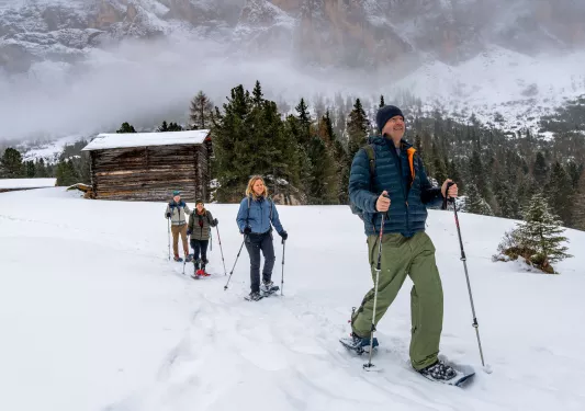 Group of hikers walking through a snowy valley with a wooden cabin in the back