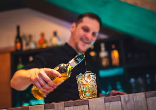 Male bartender pouring alcohol into a glass filled with ice