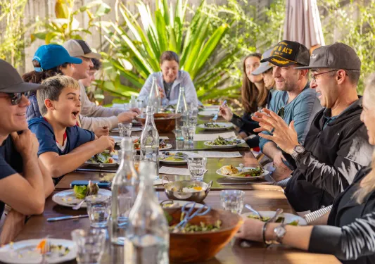 Large family sitting at a dining table, with plates of food and glass bottle of water