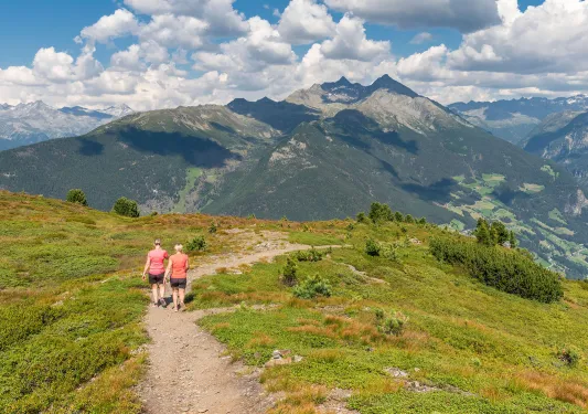 Two women hiking on a trail with mountains and clouds in the distance