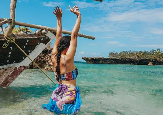 Woman standing in the water along the coast, with her arms up in the air