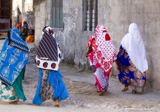 Women in Tanzania, wearing traditional clothing walking on a dirt road in a town