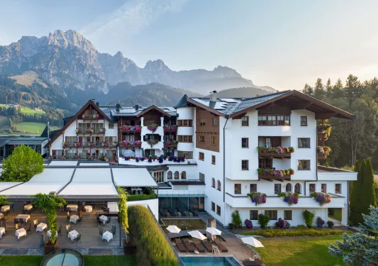 Exterior view of white and brown hotel building with large mountains in the background