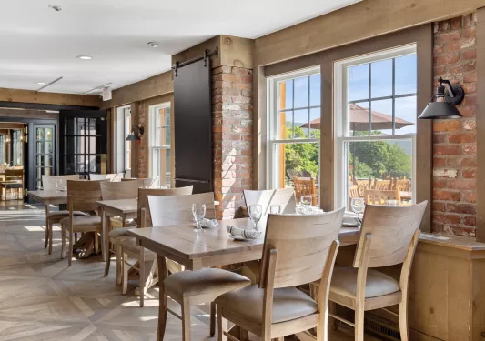 Restaurant dining area with cushioned, beige chairs and exposed brick walls