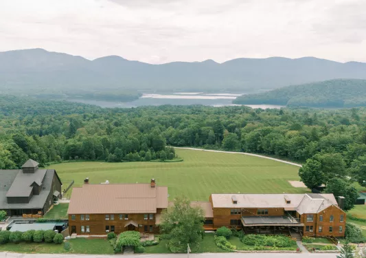 Sky view of two large, brown buildings facing a large forest