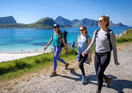 Three women walking on a dirt trail with a large lake in the background