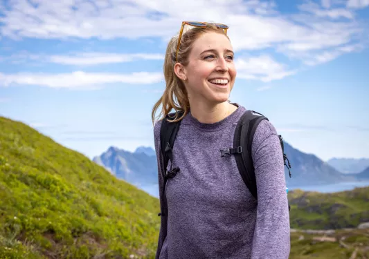 Woman smiling while wearing a backpack in the middle of a valley