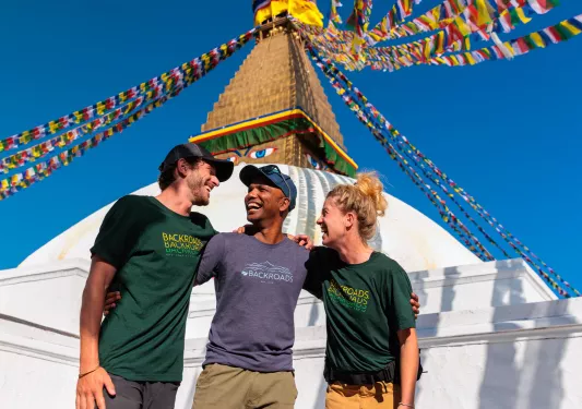 Two men and one woman hugging in front of a large statue