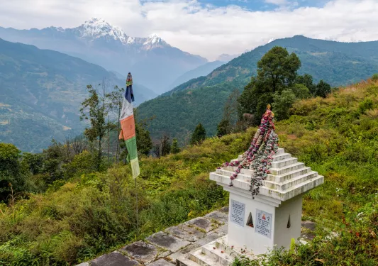 Top of a grassy hill with a stone statue and a colorful flag beside it