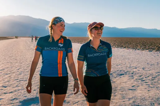 Two guests in BR jerseys walking along a sandy bank.