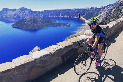 Guest cycling and gesturing towards Crater Lake on her right.