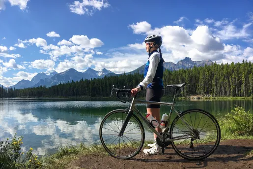 Guest standing next to bike, looking out to large lake, mountains beside them.