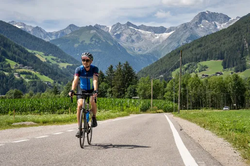 Guest cycling down mountain road, numerous peaks in background.
