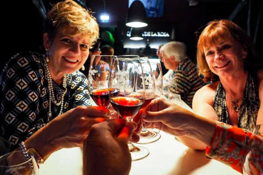 People saying cheers with glasses of red wine.