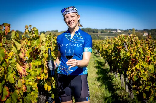 Leader among grapevines, holding wine bottle, glass.