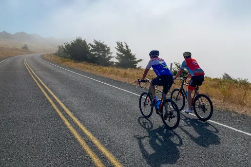 Two guests cycling up foggy road.