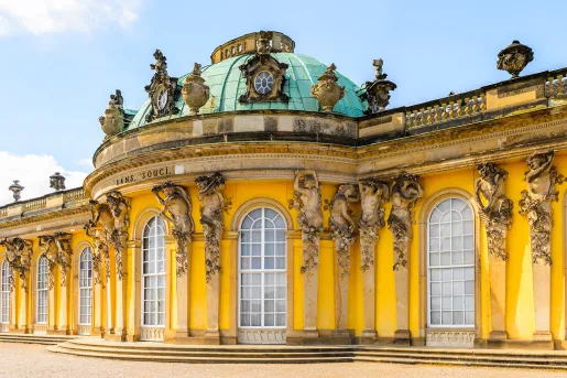 Sans Souci building in Germany, bright yellow decorated with statues of cherubs.