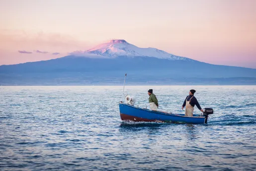 Two locals on boat during sunset, large mountain in distance.
