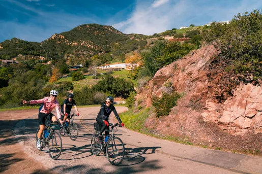 Three guests rounding corner, one pointing towards camera, Cali hills in background.