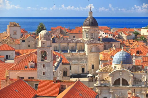 Wide shot of Dubrovnik coastline, blue ocean, white and tan houses.