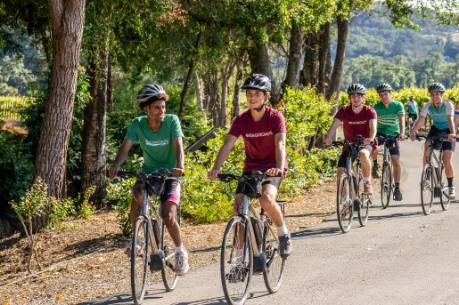 Five young guests biking down forest road, grapevines.