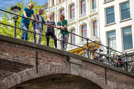 Four guests on brick bridge, large extravagant building behind them. 
