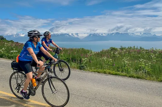 Two guests on road, cycling next to large lake. 