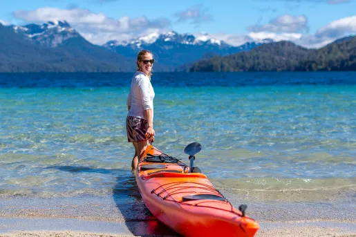 Guest pulling their kayak out to sea, large mountain range behind her.