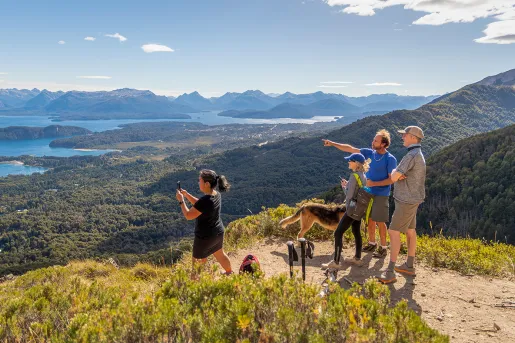 Four guests and dog on mountaintop, overlooking rivers, streams, forests, other mountains.