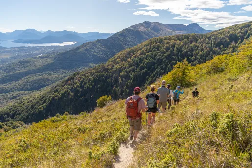 Group of guests walking down hillside, mountains, river in distance.